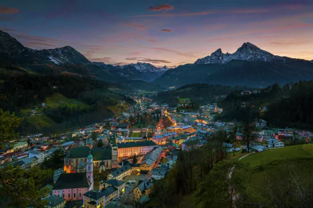 HD desktop wallpaper featuring a picturesque city nestled in a Bavarian valley, Germany, surrounded by majestic mountains at dusk.