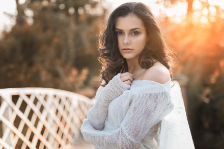 A brunette woman with brown eyes poses on a white bridge with soft sunlight and a blurred natural background, captured with a shallow depth of field.