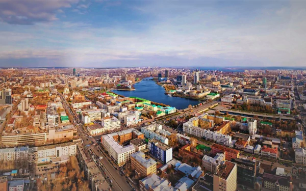 A vibrant cityscape of Yekaterinburg, Russia, showcasing the urban architecture and a river winding through the city under a partly cloudy sky.
