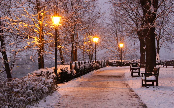 A snowy park pathway lined with benches and glowing streetlights, captured in a serene winter scene for a 4K Ultra HD PC desktop wallpaper.