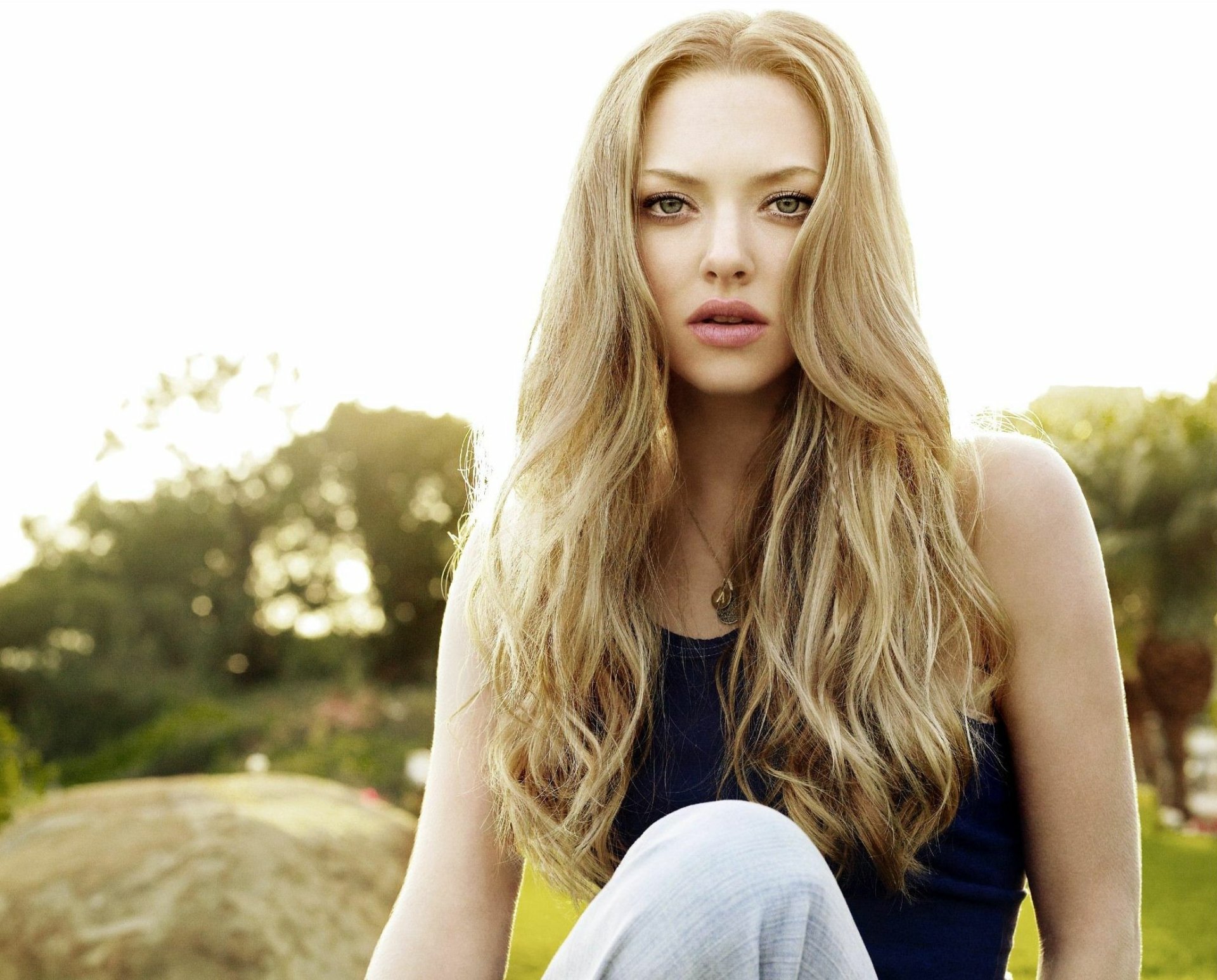 Close-up HD desktop wallpaper of a long-haired blonde woman with green eyes and soft pink lipstick, sunlit outdoor background and a calm, direct gaze.