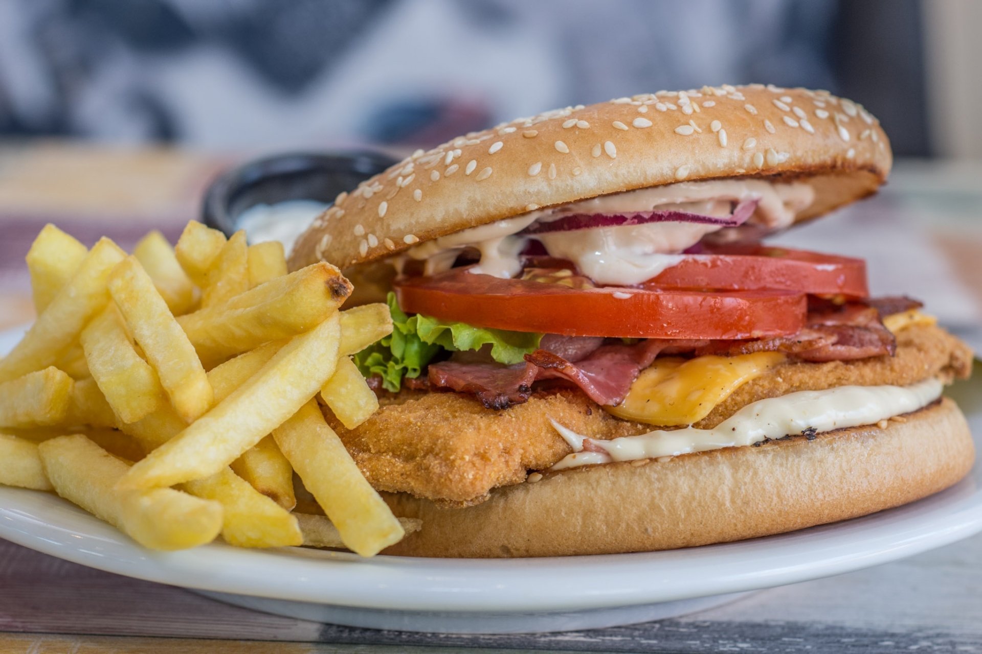 HD desktop wallpaper featuring a burger sandwich with lettuce, tomato, cheese, and bacon, served with a side of golden French fries as a delicious lunch meal.