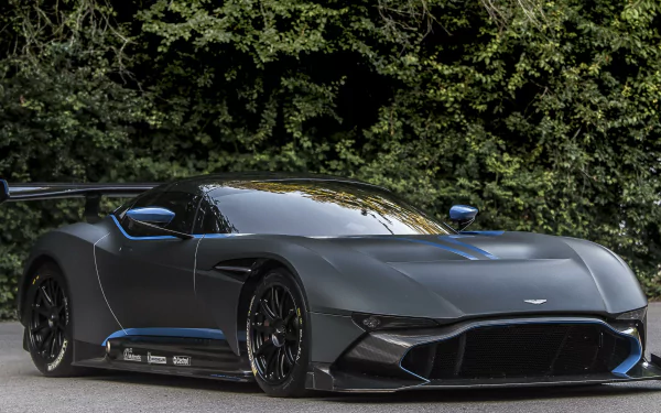 A sleek black Aston Martin Vulcan supercar with blue accents parked in front of dense greenery, shown in stunning 4K Ultra HD as a PC desktop wallpaper.