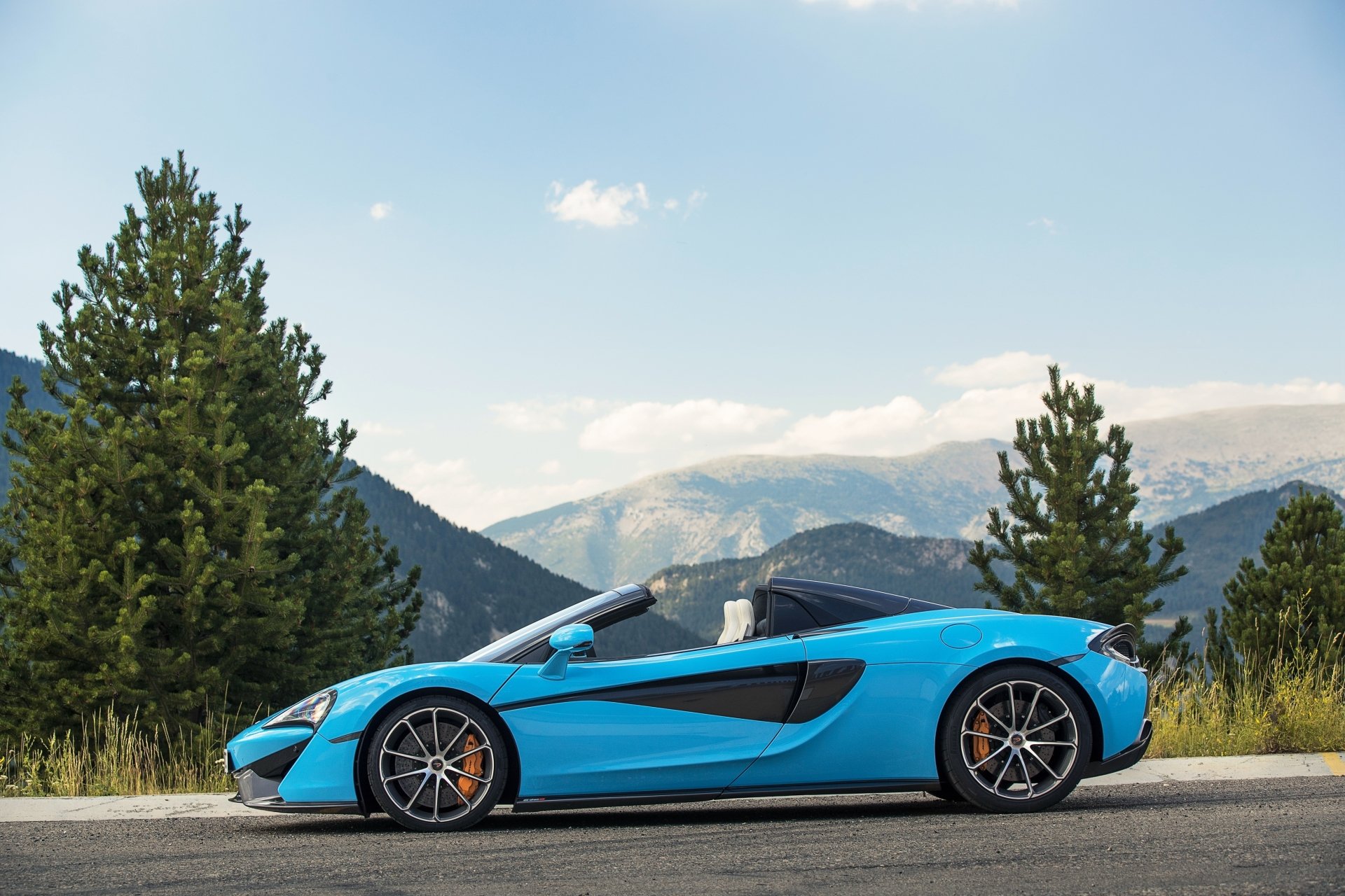 Blue McLaren 570S supercar parked on a mountain road with pine trees and distant peaks — 4K Ultra HD PC desktop wallpaper background.