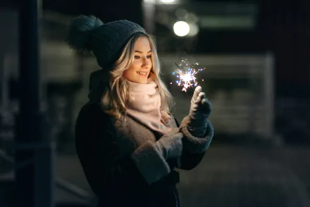 HD PC desktop wallpaper and background: smiling blonde woman in a knit hat holds a sparkler at night, model-like pose with a warm, cozy mood.