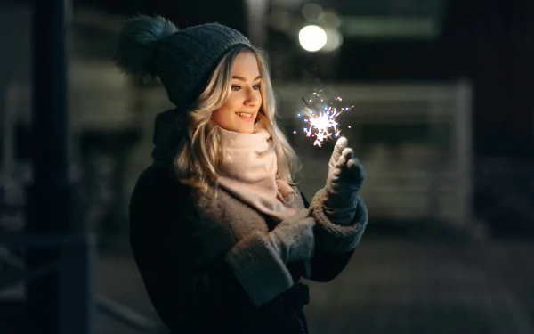 HD PC desktop wallpaper and background: smiling blonde woman in a knit hat holds a sparkler at night, model-like pose with a warm, cozy mood.
