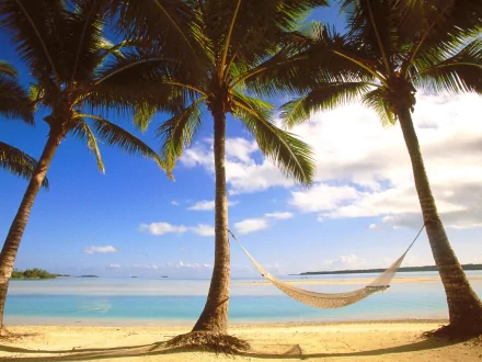 HD desktop wallpaper featuring a serene beach with a hammock strung between two palm trees. The vibrant blue sky and tranquil sea create a peaceful tropical scene.