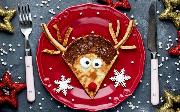 A humorous still life 4K Ultra HD wallpaper featuring a crêpe decorated as a reindeer on a red plate with snowflake-shaped accents and festive gold and red stars.