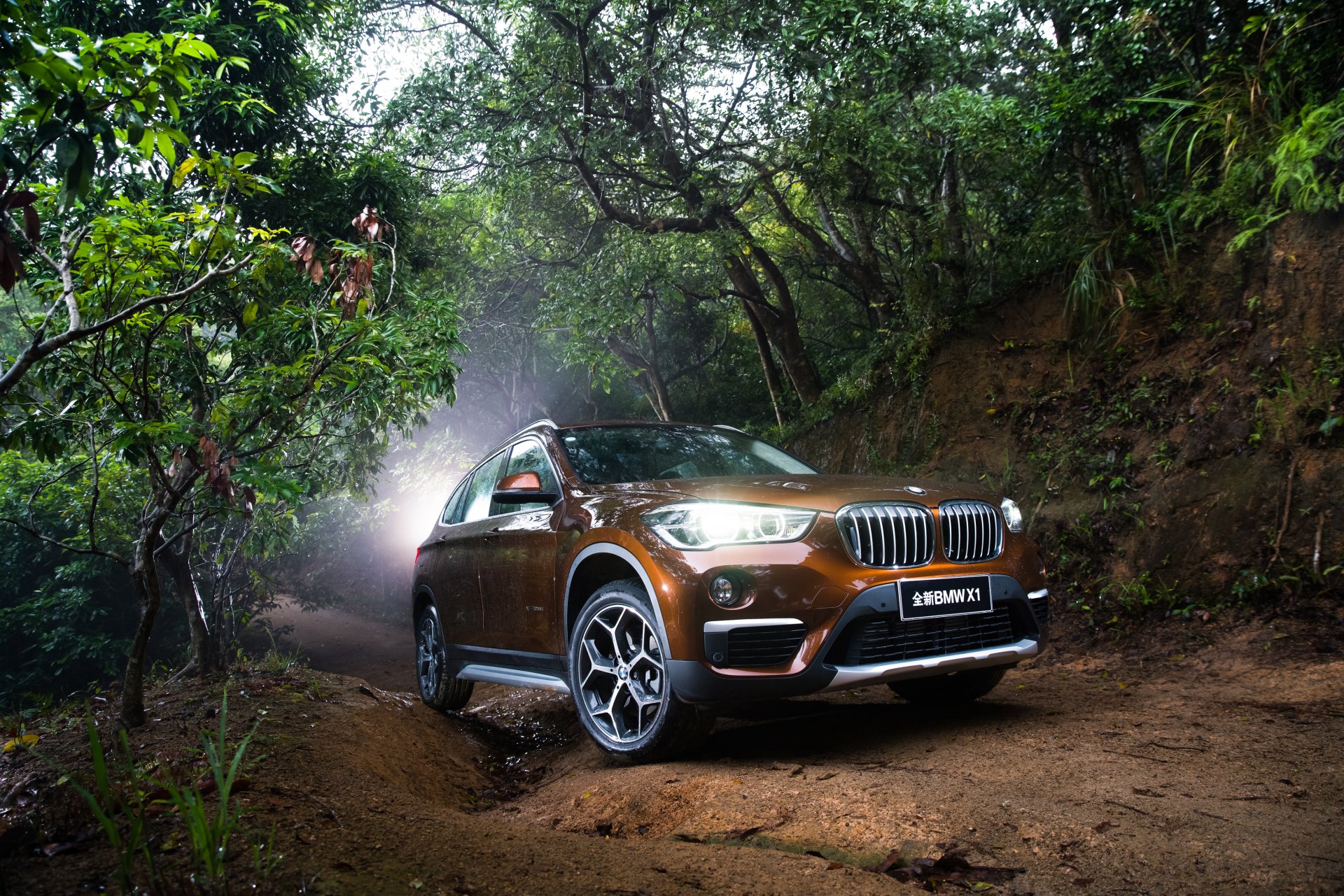 Orange BMW X1 SUV on a muddy forest trail, 4K Ultra HD PC desktop wallpaper background showcasing the crossover's rugged stance and glossy finish.