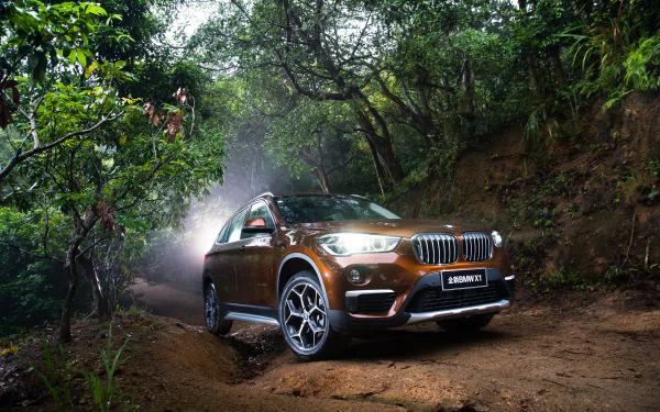 Orange BMW X1 SUV on a muddy forest trail, 4K Ultra HD PC desktop wallpaper background showcasing the crossover's rugged stance and glossy finish.