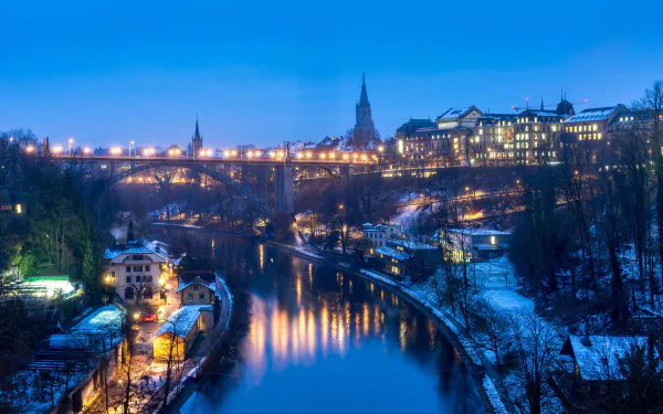 Night view of a man-made bridge over a river in Lucerne, Switzerland, with glowing town lights and snowy banks — HD PC desktop wallpaper background.
