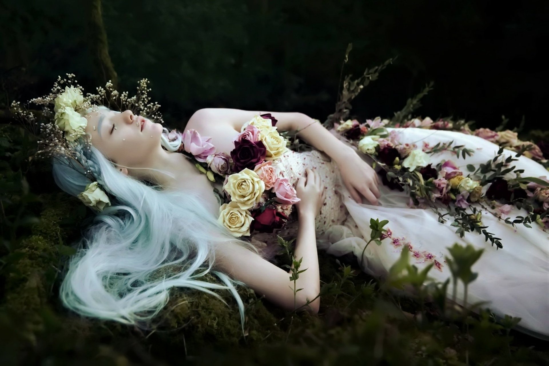 HD PC desktop wallpaper/background: a sleeping woman with long pale hair lies on moss, draped in roses and petals with a floral crown, evoking a dreamy, melancholic mood.