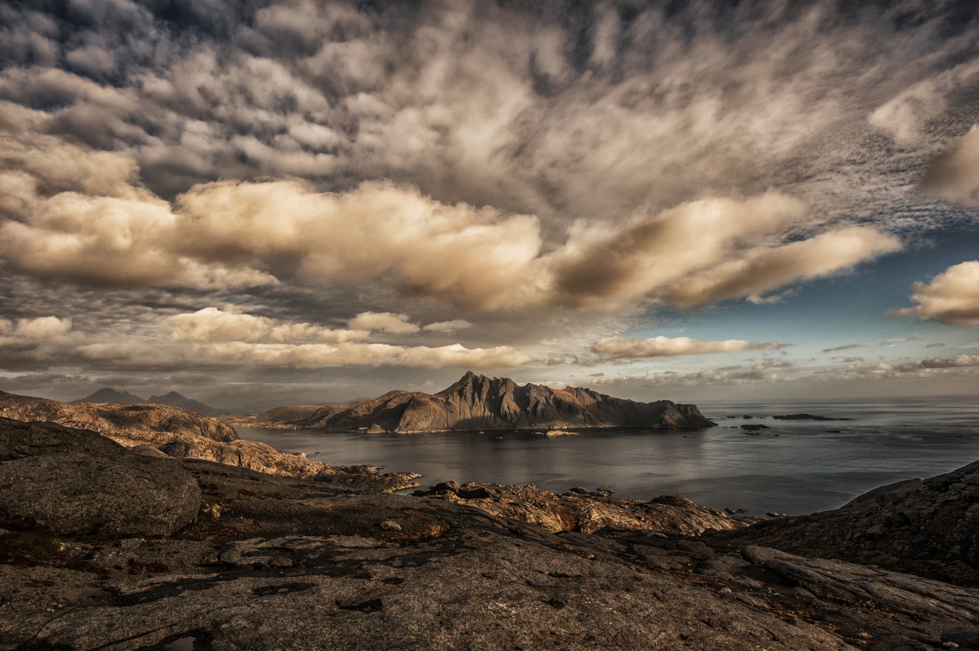 HD desktop wallpaper featuring a stunning landscape with a mountain range on the horizon under a dramatic sky filled with scattered clouds.