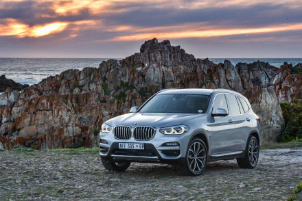 Silver BMW X3 SUV parked on a rocky coastal overlook at sunset — 4K Ultra HD PC desktop wallpaper/background.