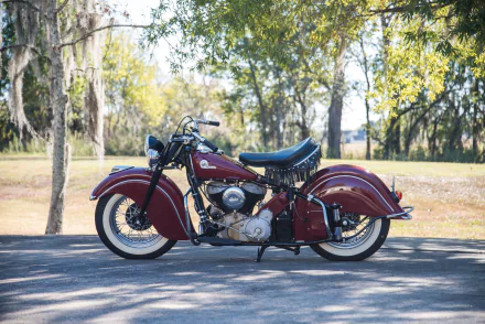 HD desktop wallpaper featuring a classic red Indian Chief motorcycle parked on a sunlit road with trees in the background.