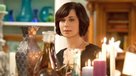 HD PC desktop wallpaper from the TV show Good Witch: a dark‑haired woman sits among lit candles and glass bottles in a warm, cozy interior.