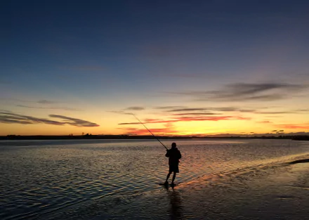 Silhouette of a fisherman casting a line into a river at sunset, captured in HD for a serene sports-themed PC desktop wallpaper.