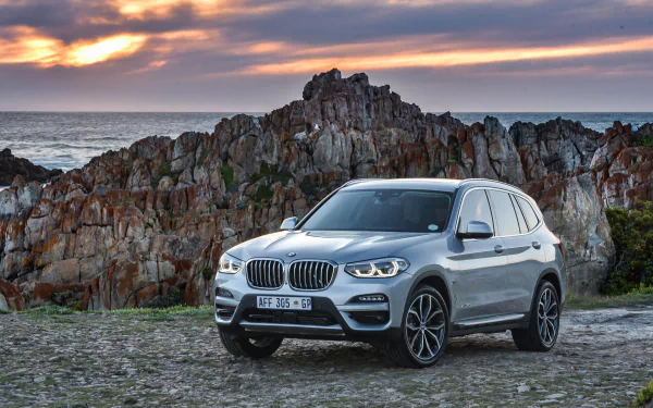 Silver BMW X3 SUV parked on a rocky coastal overlook at sunset — 4K Ultra HD PC desktop wallpaper/background.