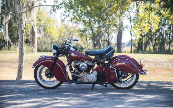 HD desktop wallpaper featuring a classic red Indian Chief motorcycle parked on a sunlit road with trees in the background.