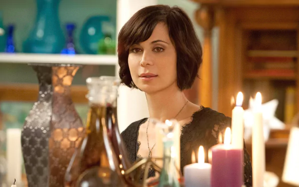 HD PC desktop wallpaper from the TV show Good Witch: a dark‑haired woman sits among lit candles and glass bottles in a warm, cozy interior.