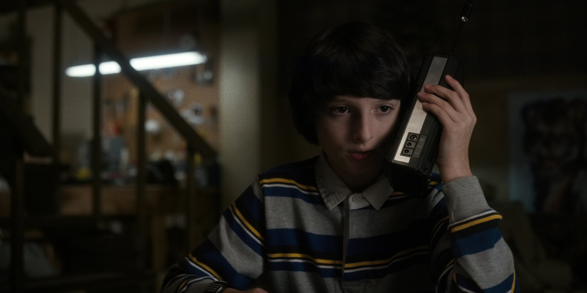 2K desktop wallpaper: a boy in a striped sweater holds a cordless phone in a dim basement, evoking the moody TV show Stranger Things.