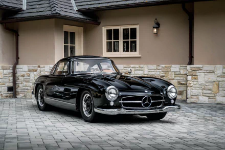 Black Mercedes-Benz 300SL grand tourer parked on a stone driveway in front of a beige house, showcased as a high-definition PC desktop wallpaper.