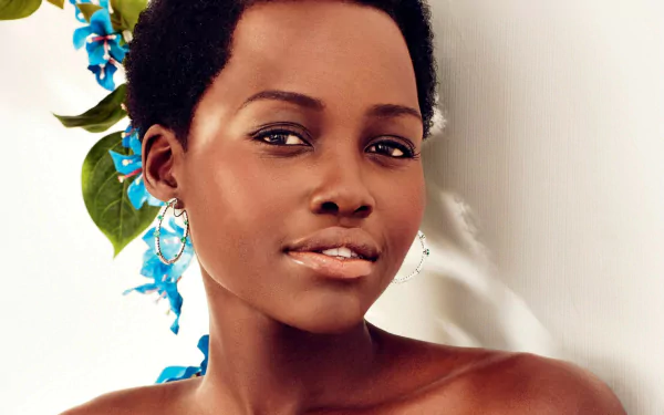 HD desktop wallpaper: close-up portrait of a smiling woman with short natural hair and hoop earrings, soft lighting and blue floral accents against a pale background.