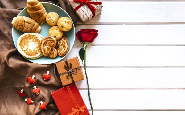 A red rose, wrapped gifts, and a plate of viennoiserie on a white wooden table create a romantic Valentine’s Day breakfast still life in 4K Ultra HD.