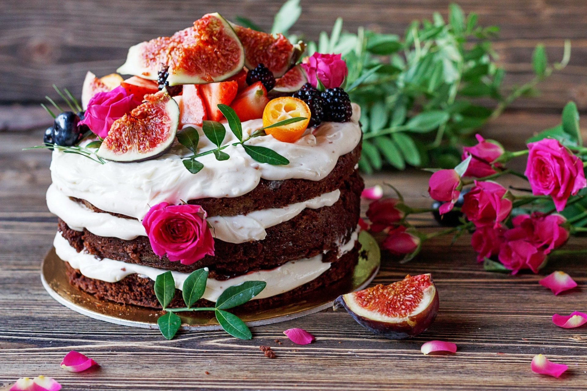 HD PC desktop wallpaper - still life of a rustic layered cake topped with figs, berries and pink roses, surrounded by rose petals and greenery on a wooden background.