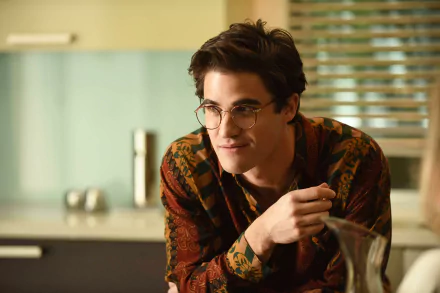 A high-definition desktop wallpaper from the TV show American Crime Story, featuring a young man in glasses, engaged in conversation in a modern kitchen setting.