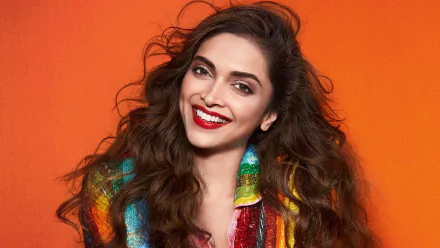 Portrait of Deepika Padukone, Indian Bollywood actress with long brunette hair, brown eyes, and bright lipstick, smiling against an orange background in 4K Ultra HD.