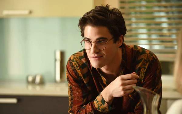 A high-definition desktop wallpaper from the TV show American Crime Story, featuring a young man in glasses, engaged in conversation in a modern kitchen setting.