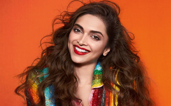 Portrait of Deepika Padukone, Indian Bollywood actress with long brunette hair, brown eyes, and bright lipstick, smiling against an orange background in 4K Ultra HD.