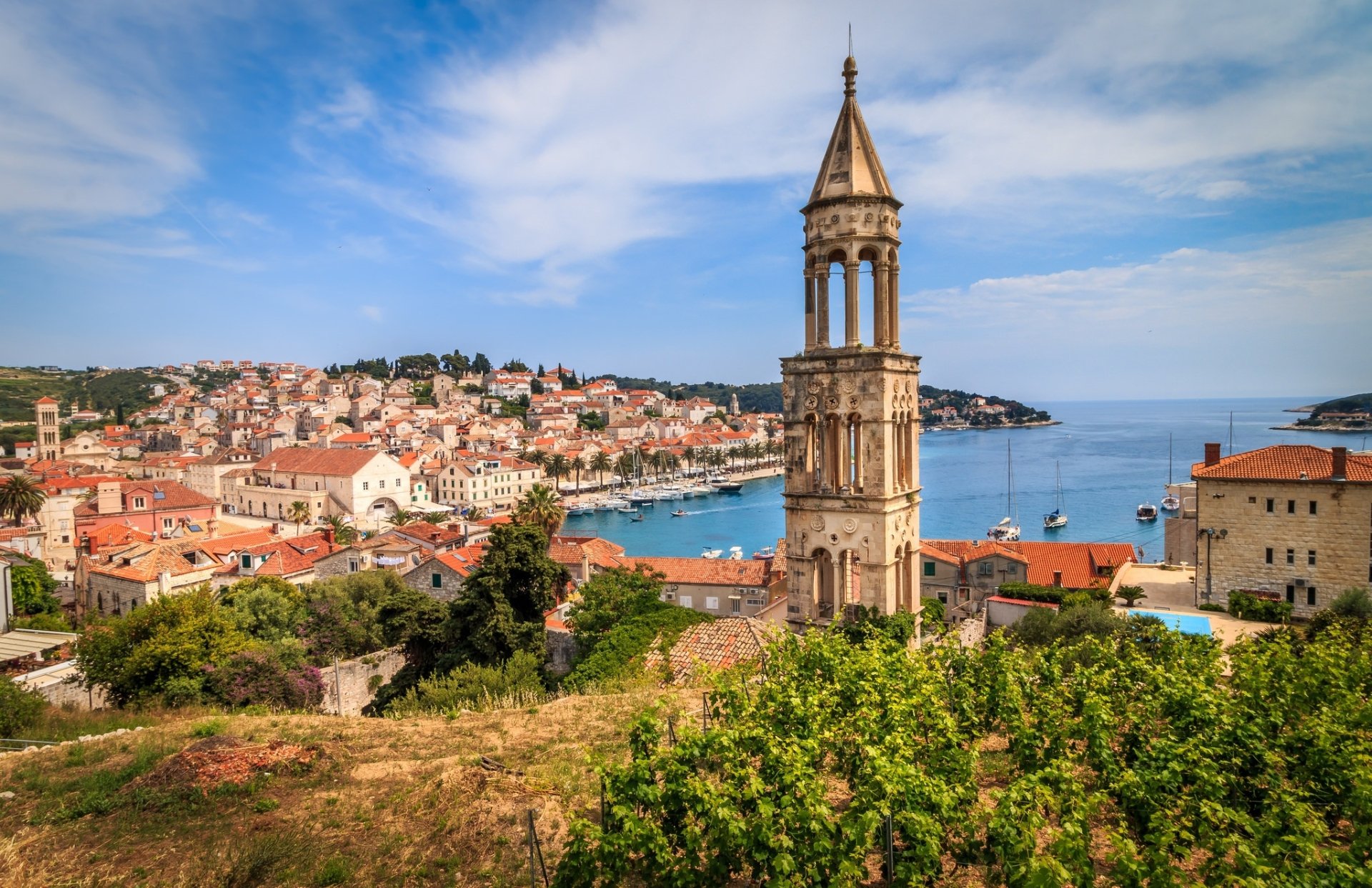 HD desktop wallpaper of a Croatian coastal town: red-roofed houses and a prominent man-made bell tower overlooking the harbor and blue Adriatic Sea.
