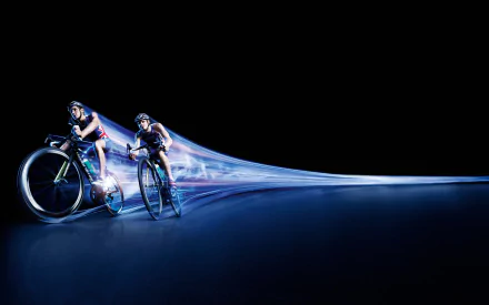 2K Quad HD PC desktop wallpaper showing two cyclists in time-lapse motion with luminous trails racing across a dark background, bicycle cycling sports imagery.
