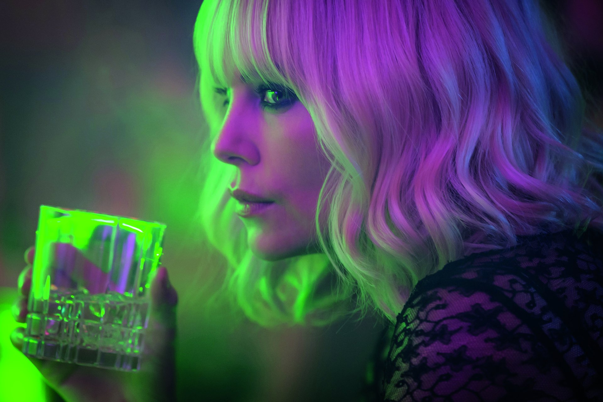 Close-up of Charlize Theron from the movie Atomic Blonde, illuminated by neon green and purple lighting, featured in a 4K Ultra HD PC desktop wallpaper.