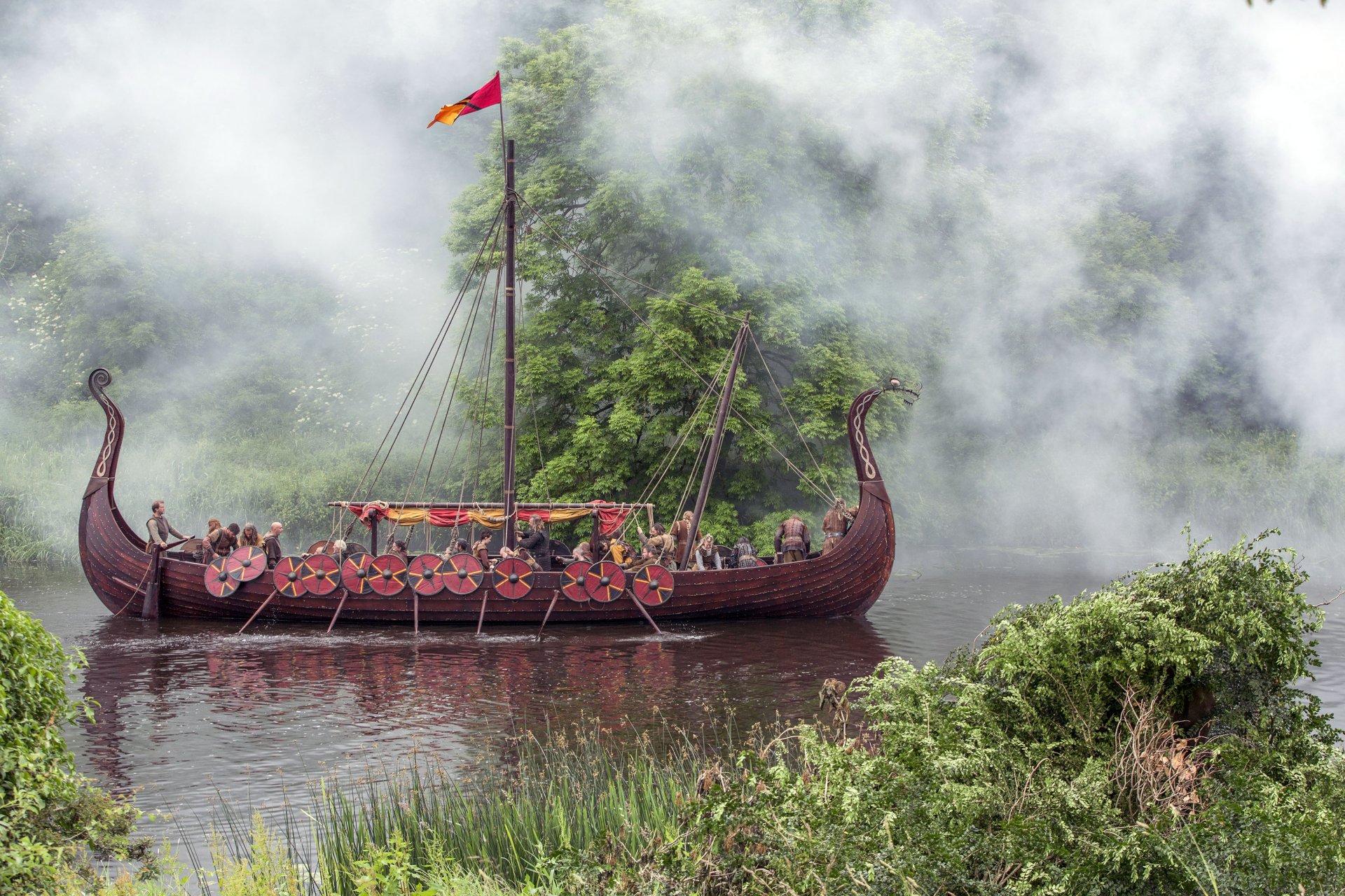 HD desktop wallpaper featuring a Viking longship from the TV show Vikings (2013) sailing through misty waters surrounded by lush greenery.