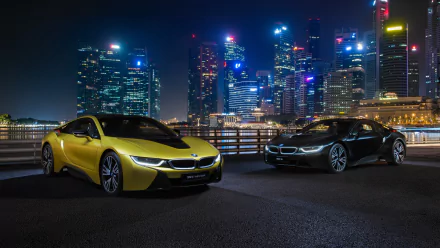 Two BMW i8 supercars, one yellow and one black, parked at night with a brightly lit city skyline in the background. 4K Ultra HD desktop wallpaper.