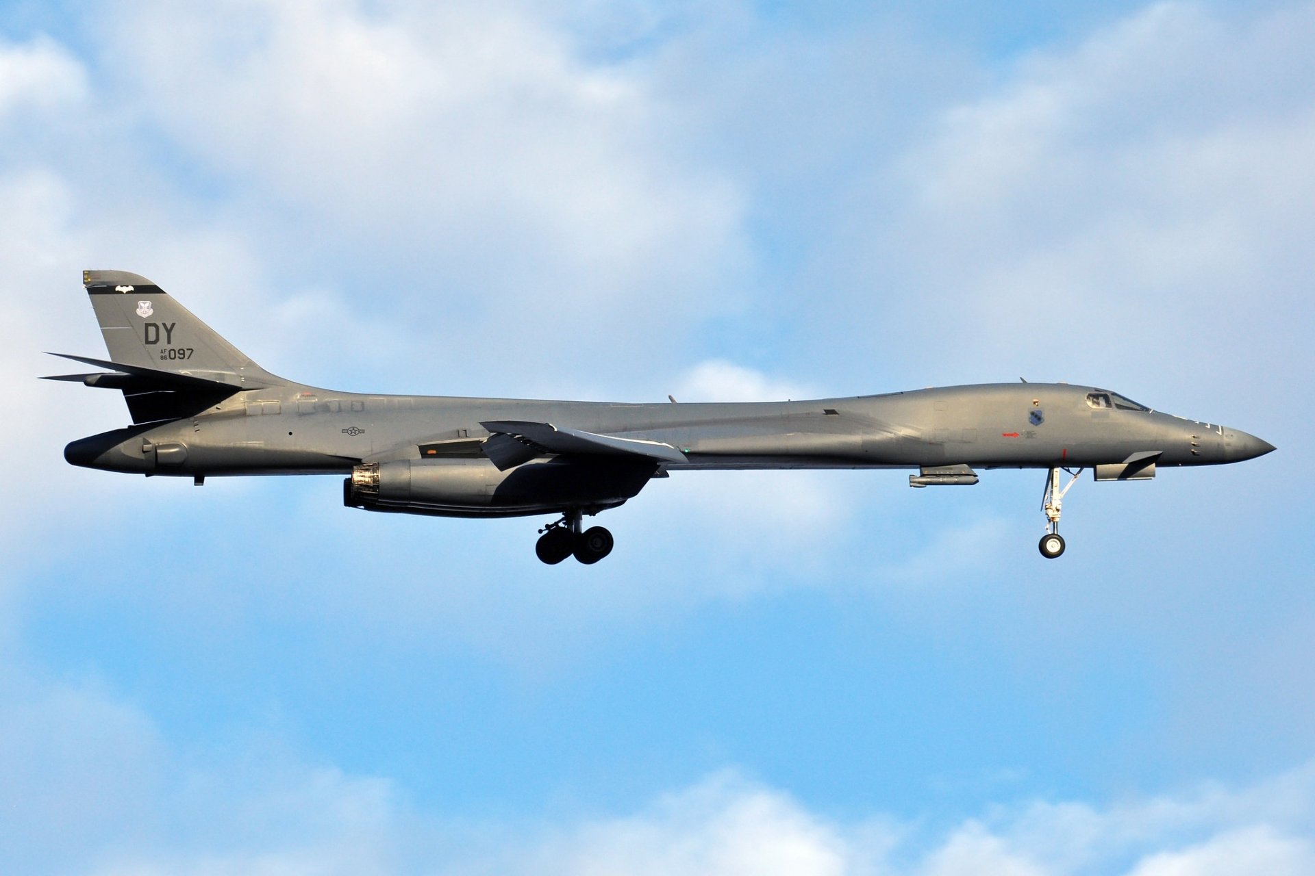HD desktop wallpaper featuring a Rockwell B-1 Lancer military bomber warplane in flight against a blue sky with clouds.