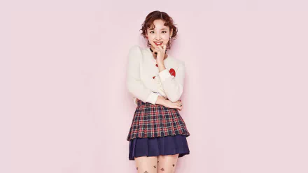 Smiling young Korean woman with brown eyes and red hair in a plaid skirt and white sweater on a pink background — K-pop–style HD desktop wallpaper.