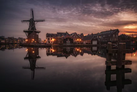 A serene HD image of Haarlem, Netherlands, featuring a windmill, buildings, and houses reflecting on a calm lake at dusk. The peaceful townscape is beautifully captured as desktop wallpaper and background.