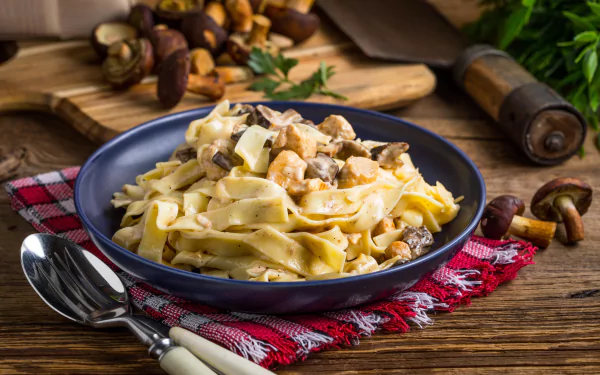 A close-up of a mushroom pasta meal in a blue bowl on a rustic wooden table, styled as an 8K Ultra HD PC desktop wallpaper featuring still life food photography.