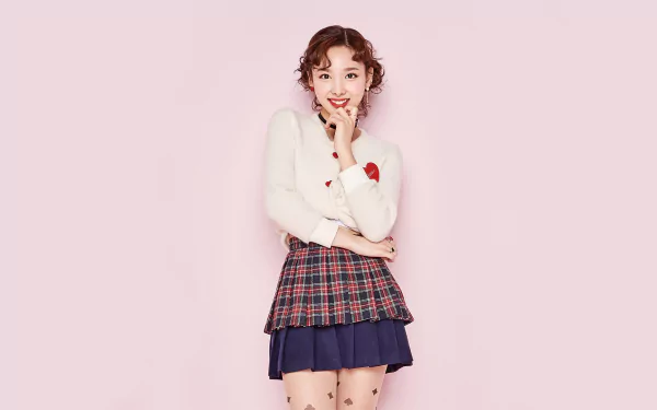 Smiling young Korean woman with brown eyes and red hair in a plaid skirt and white sweater on a pink background — K-pop–style HD desktop wallpaper.