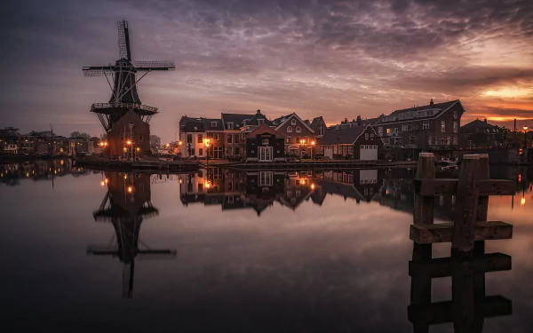 A serene HD image of Haarlem, Netherlands, featuring a windmill, buildings, and houses reflecting on a calm lake at dusk. The peaceful townscape is beautifully captured as desktop wallpaper and background.