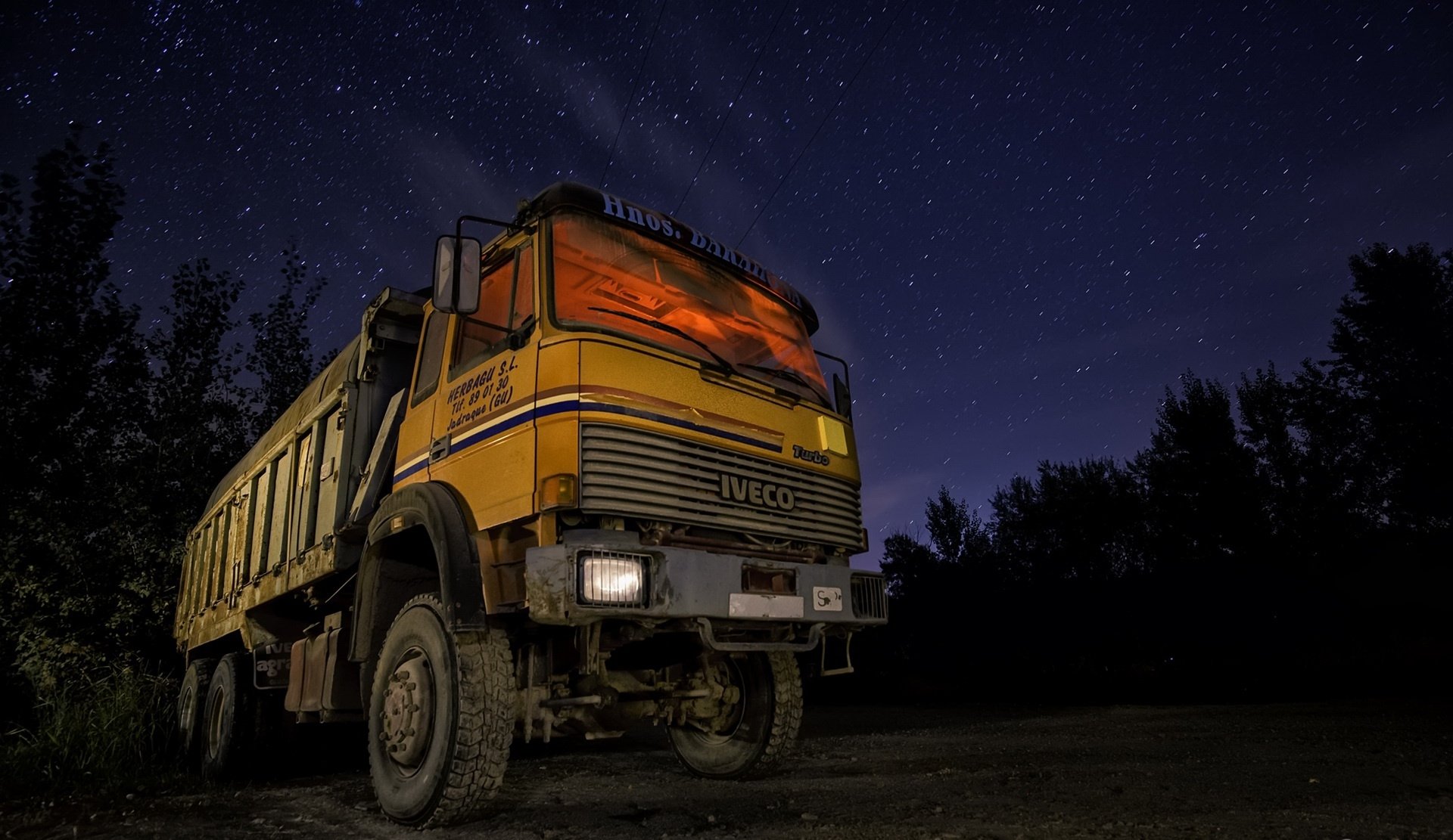 A yellow Iveco truck parked at night under a starry sky, captured in HD for a desktop wallpaper background.