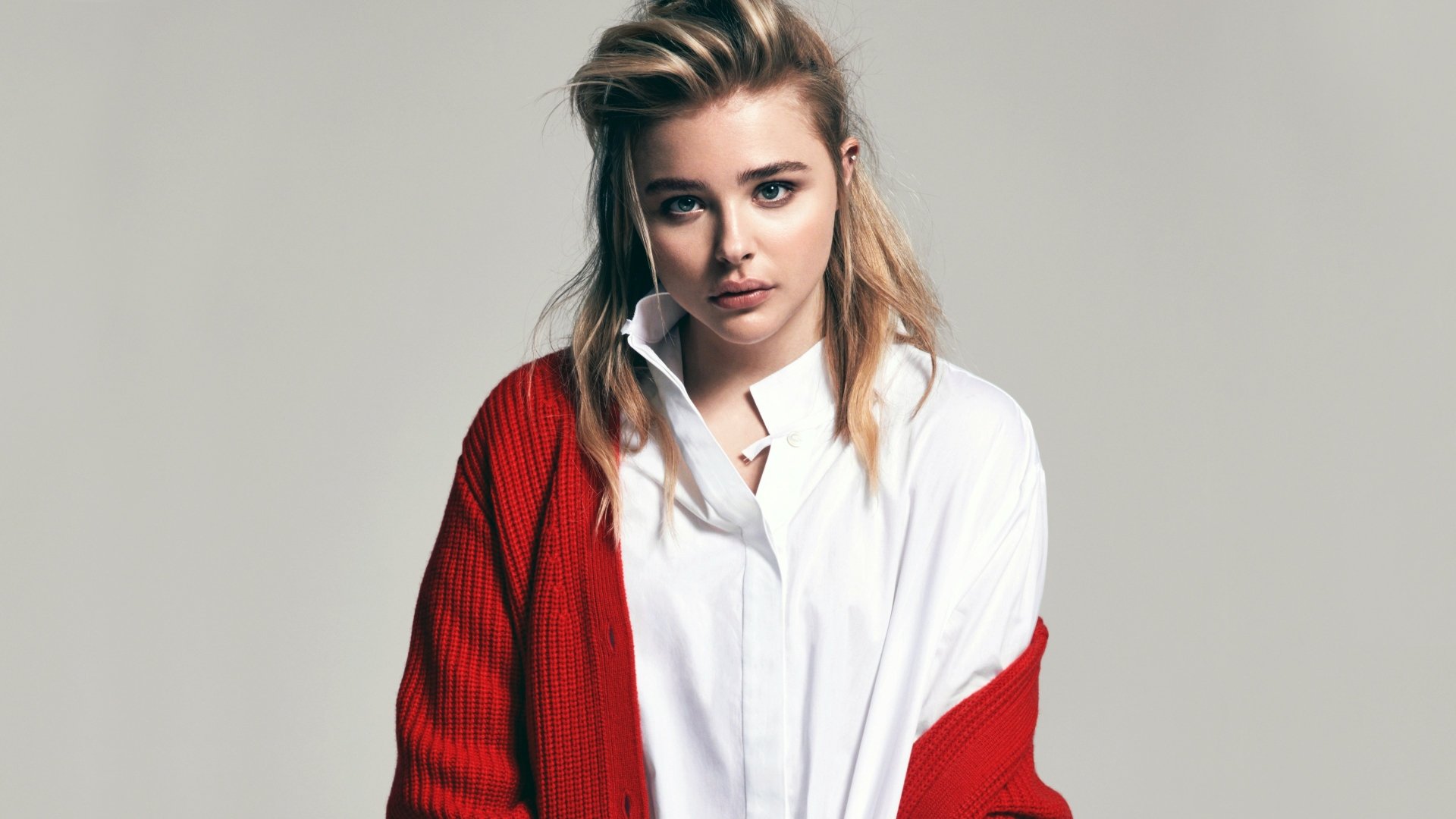 A high-definition desktop wallpaper featuring actress Chloë Grace Moretz with long blonde hair, blue eyes, wearing a red cardigan over a white shirt.