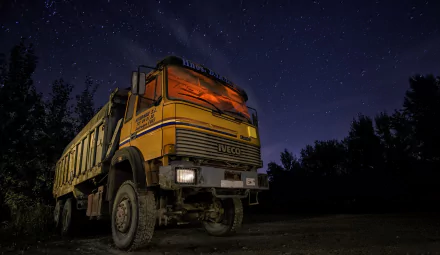 A yellow Iveco truck parked at night under a starry sky, captured in HD for a desktop wallpaper background.