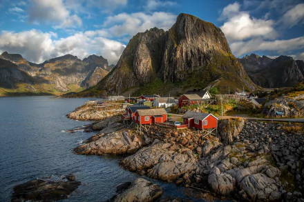 Scenic view of Reine in Lofoten, Norway, featuring traditional red houses by a lake with dramatic mountains under a partly cloudy sky, captured in high-definition photography.