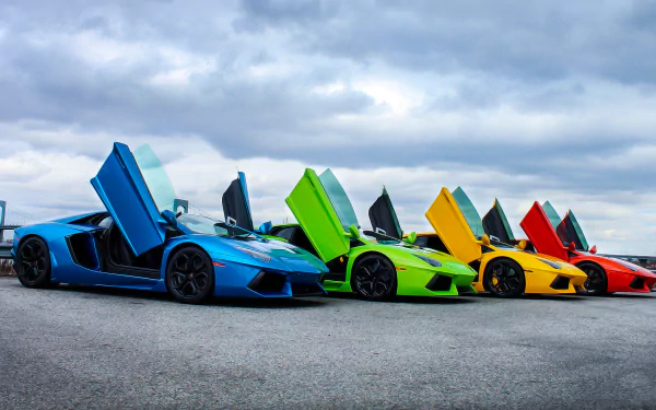 A vibrant HD desktop wallpaper featuring a lineup of Lamborghini Aventadors in blue, green, yellow, and orange, with their doors stylishly open against a cloudy sky backdrop.