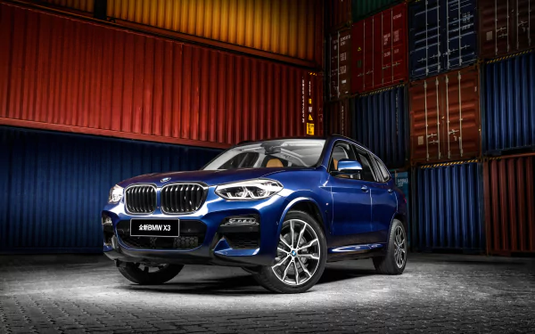 A striking blue BMW X3 SUV is showcased against stacked shipping containers, captured in 4K Ultra HD as a desktop wallpaper and background.